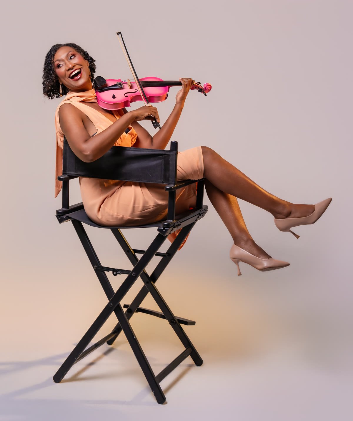 Melanie riendo mientras toca su violín rosado, sentada en una silla de director