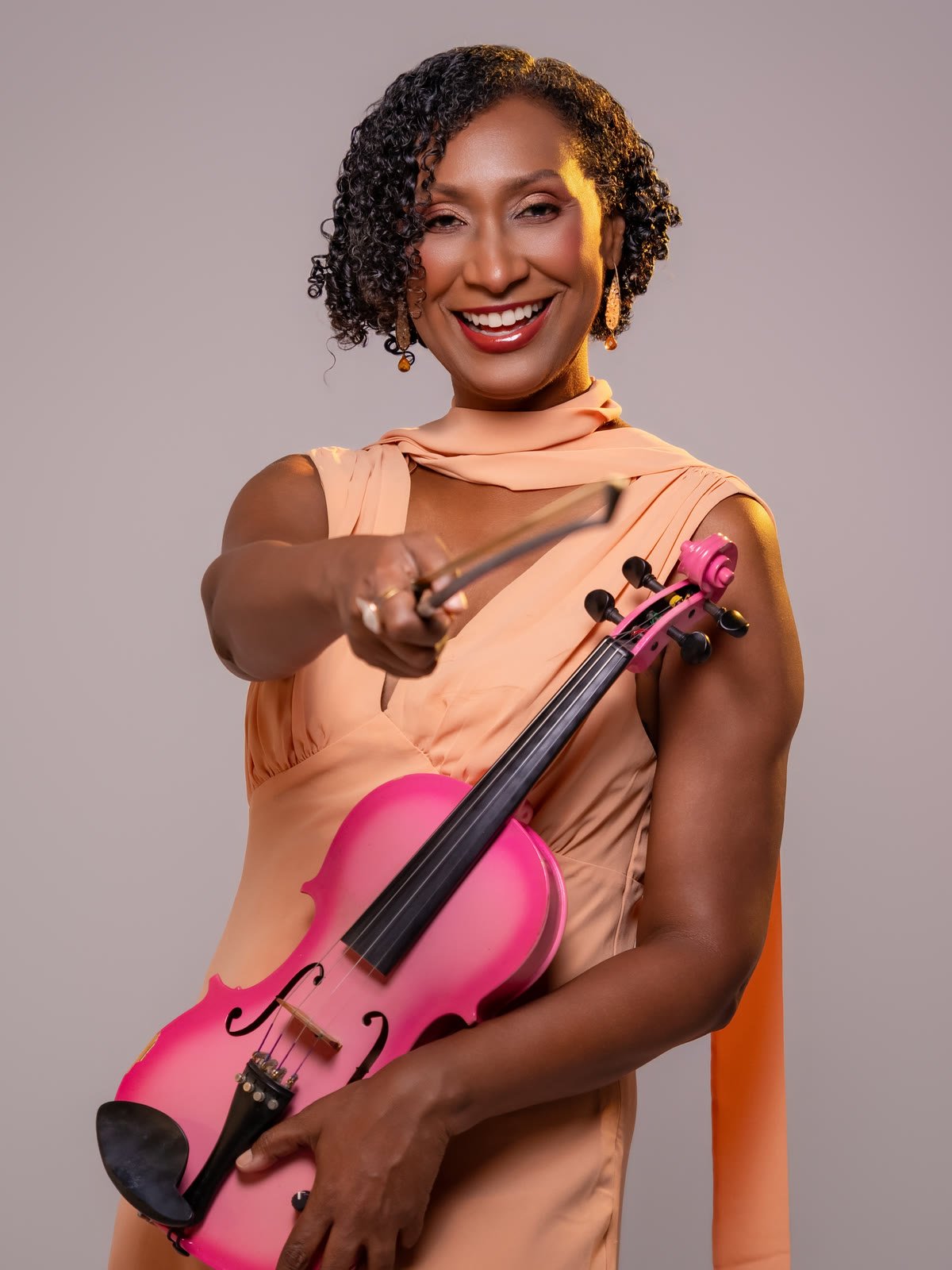 Melanie Taylor sonriendo, con su violín rosado en el brazo y el arco extendido hacia la cámara